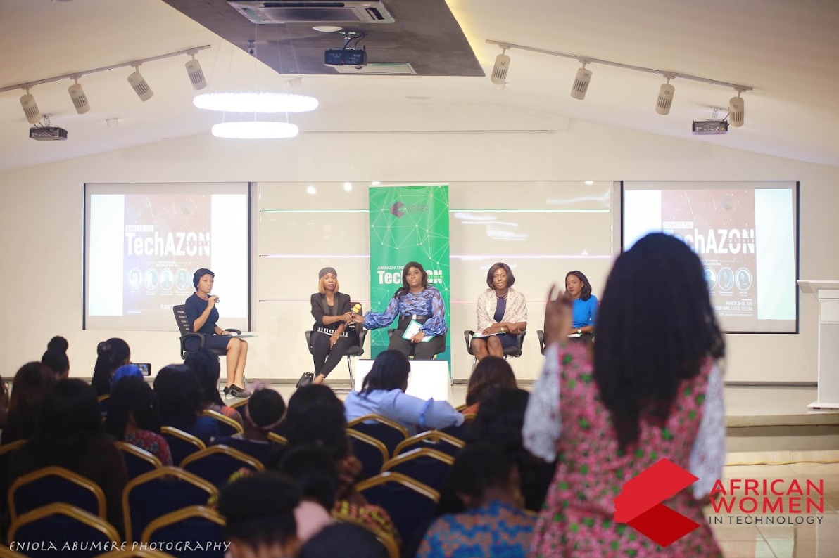 Ommo Clark seated on a panel at the African Women in Technology Conference (TechAZON) in Lagos, with the event's branded screens visible behind the panellists