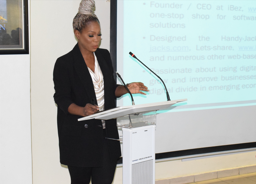 Ommo Clark speaking at a podium during a Fidelity Bank Lagos training program, with a slide showing her bio displayed on the projection screen behind